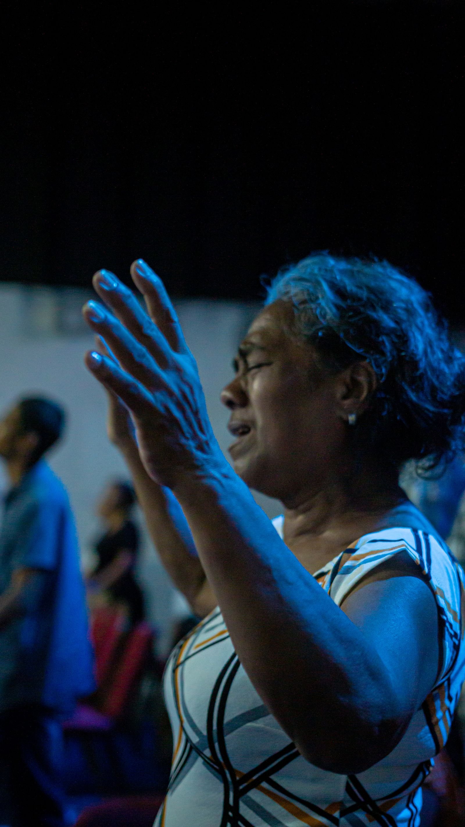 A woman praying with raised hands under blue light