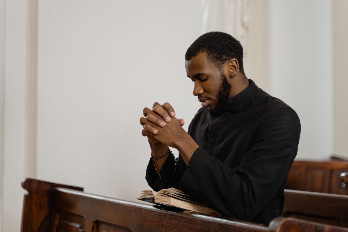 A man praying with folded hands in a church pew